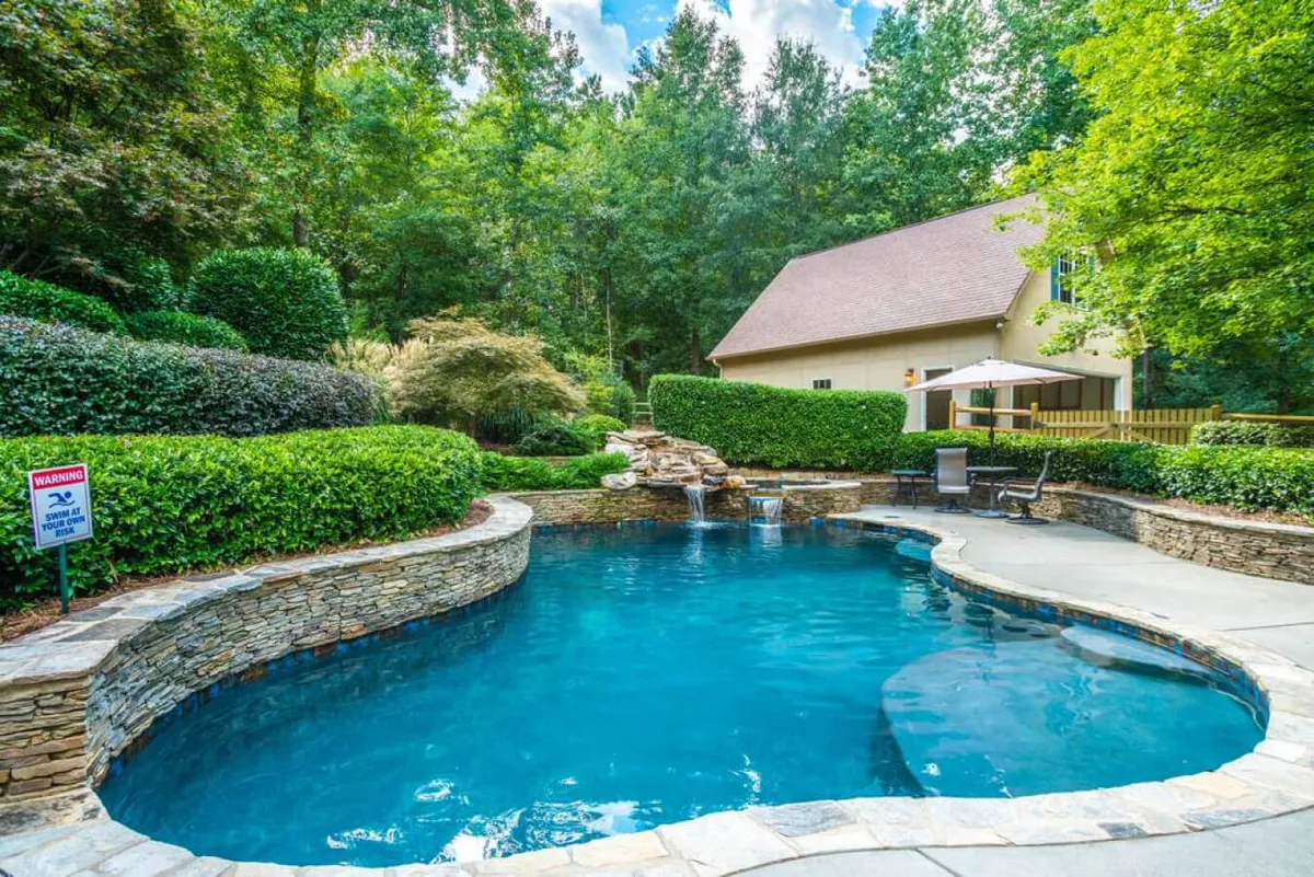 This image captures the villa's swimming pool complete with a waterfall feature, surrounded by lush greenery and a spacious patio area. The serene setting hints at both day and evening enjoyment for families returning from local adventures.