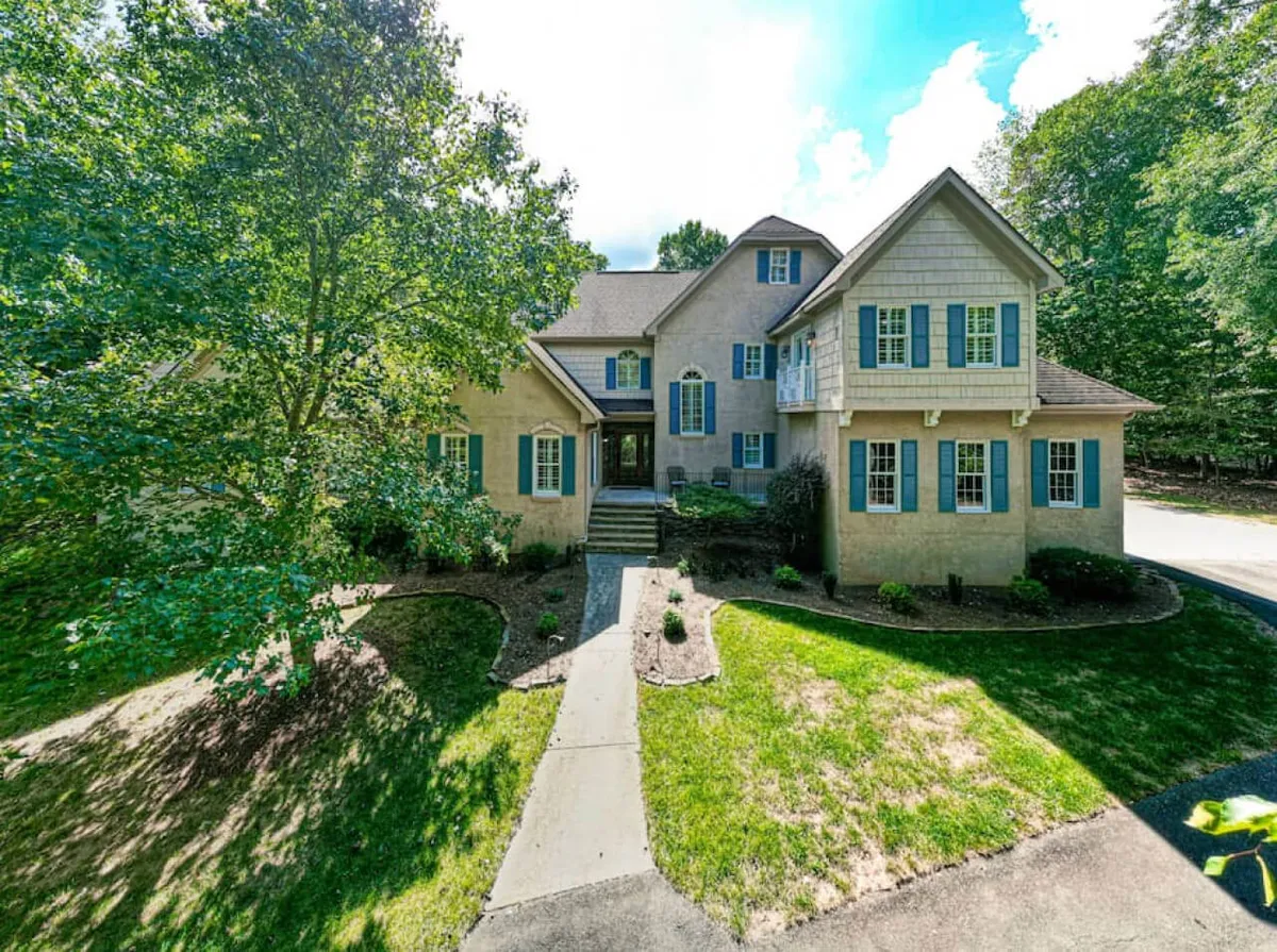 An inviting view of the home's front entrance, highlighted by a landscaped garden, large windows, and dormer features, suggesting a warm welcome and connection to the surrounding neighborhood.