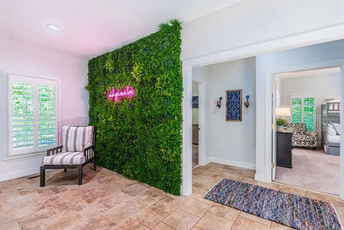 A lively interior corner featuring a green wall with a neon sign, a comfortable chair, and a plush rug. The vibrant backdrop is ideal for memorable group photos or casual conversations, exuding both comfort and whimsy.
