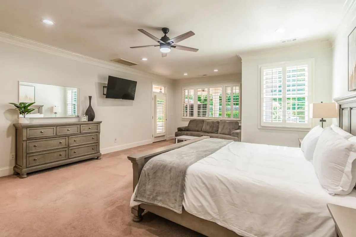 A tranquil bedroom featuring a king-sized bed with premium linens, a comfortable sofa, a dresser, and a window with shutters letting in natural light. The thoughtful arrangement creates a feeling of spaciousness and comfort, perfect for relaxation after a long day.