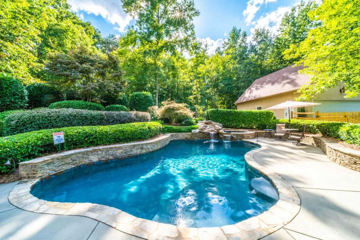 A tranquil outdoor pool is surrounded by lush greenery and features a soothing waterfall. The scene is set for swimming, sunbathing, and hosting social gatherings, with a relaxed and serene ambiance that invites guests to unwind or celebrate together.