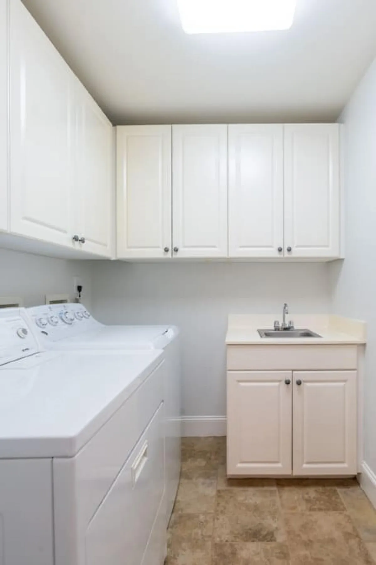 A neatly organized laundry area featuring a washing machine, dryer, a utility sink, and cabinets for storage. The space is brightly lit and designed for efficiency, providing all the essentials needed for in-unit laundry routines.