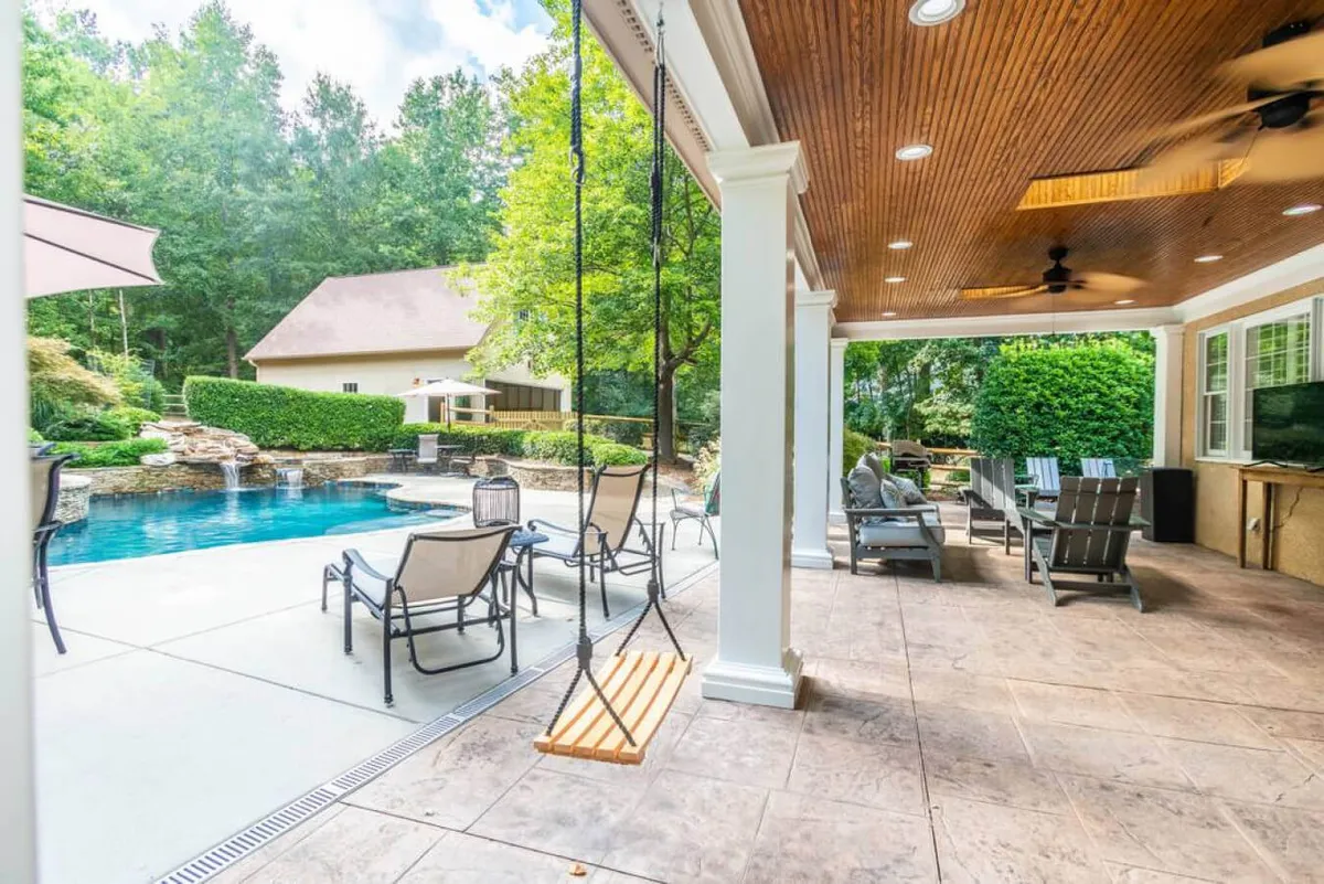 An expansive exterior scene featuring a sparkling swimming pool, a cozy swing, outdoor seating, and lush landscaping. The inviting patio area is visible, ideal for swimming, lounging, or grilling, reflecting the 'resort-style' vibe mentioned in the text.